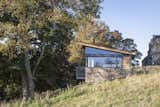 The lightweight steel, glass and timber structure sits above a heavy stone plinth.