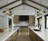 A GRAND COOKING AND ENTERTAINING EXPERIENCE
Each space in the home provides a little wow factor, none more evident than in the kitchen. The vaulted ceiling and views of the lake offer a hint of drama while the materials palette creates a feeling of warmth and a sense of intimacy. Rich woods and clean whites are accented by a combination of metal finishes. The work zone boasts a custom subtly sloped hood with a gradient finish. Full quartzite countertops are inviting surfaces for guests, sleek to the touch, and perfect for entertaining.