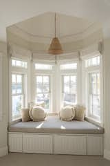 The window niche in the primary bedroom is a great spot to take a quiet moment. Fussy drapery and floral upholstery were replaced with woven wool fabric and linen roman shades, for a more relaxing, hygge vibe. 