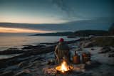A person sitting by a campfire on the beach at night, enjoying the warmth and tranquility of the flickering flames.