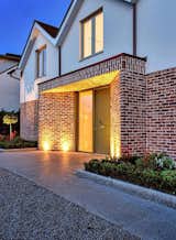 Warm Welcome: Subtly integrated into the pavement, uplighters illuminate the splayed brick piers and floating brick soffit, bestowing a gracious and warm ambiance upon the distinctive entrance of the custom new build dwelling