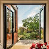 The playroom patio beckons with double doors wide open, seamlessly connecting the indoor space to a second patio. Overlooked by the kitchen sink window, a timber threshold step extends a warm invitation to step outside and enjoy the delightful play area.