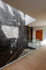 The central staircase in Pierre de Varennes stone provides the perfect feature wall and showcases the floating oak stairs and a custom cascading chandelier by Canadian designer Randy Zieber in sand-cast bronze and alabaster, spanning all three floors of the home and accentuating the height.