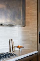 The curved design element is repeated in the kitchen backdrop, where an outward facing curved stained bronze exhaust hood contrasts the inward curving marble backdrop and ties in with several bronze details throughout the kitchen.