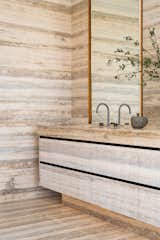 The double shower is framed by bronze doors and the double travertine sink adds tactile interest through a combination of open-pored matte fluted and smooth finishes, contrasted with a bronze reveal and patinated bronze Watermark taps. 