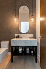 A remodeled powder room features a Venetian plaster wall and a custom iron vanity with a thick Dekton countertop. Moody RH pendant lighting and a dramatically tall mirror make this powder room a place of its own.  Photo 9 of 19 in Hollywood Hills Remodel by Belyn Studio