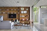 Na sala de estar, uma das paredes recebeu a estante de em freijó natural e o módulo baixo com portas de espelho, acomodando a TV, livros e outros pertences da família. A sala de estar ainda tem conforto e design garantidos pela Poltrona Mole, assinada por Sérgio Rodrigues. Outras peças complementam o ambiente, como a luminária de piso Magneto e o abajour Lumière, ambos da Lumini.