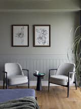 Wainscoting adds a touch of elegance, while the plain grey walls above the wainscoting provide a balanced backdrop, while botanical artwork by the talented artist Rudrani.