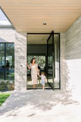 Mother and son hold hands in front of open RAM pivot door to luxury home. 