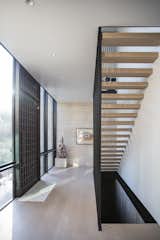 A modern entryway with unique door and floating stairs are illuminated by RAM picture windows.