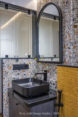 The bathroom too has been made using colourful terrazzo stone in a vertical stepped cladding format and while the chrome yellow mosaic in the shower area acts as highlight to the entire colour scheme keeping the vibe in the toilet both mature and playful. The black matt sanitary fixtures create a contrast to the given material pallet