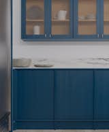 The Japandi-inspired base cabinets are paired with upper cabinets painted in a matching vibrant blue. These feature fluted glass fronts with elegant golden finger pulls, offering a subtle, veiled effect that allows a glimpse into the interior of the cabinets.