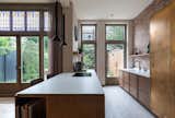 
The kitchen has an open connection to the back room where the dining and playroom sits. The kitchen island of walnut with alcoves for cookbooks provides a warm homely connecting element between the different functions.
The back wall of the kitchen is also exposed with the original red warm brick from 1906. Against this are two elements, both uniquely materialized. The tall fridge is brass and the low section with the sink has the same material as the kitchen island, walnut with a beige stone composite top. The sink has the same material as the composite top, making it sink into the kitchen worktop.