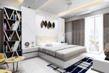 The room is light and airy, with a predominantly white and neutral colour palette. A light beige/cream coloured bed with a white bed frame sits in the center of the image. The bed has a bedspread that features a subtle patterned design consisting mainly of stripes on a light cream/beige. 
A dark-grey, geometric bookshelf occupies the left side of the image.  The shelves are a mix of varying depths and angles, creating a visually interesting pattern. Books are visible on the shelves. 
A small, light-coloured, roundish coffee table with metal legs sits in front of the bookshelf. It has a light beige/tan top. A mustard/yellow coloured chair and part of another matching chair are visible, located next to the table.
The wall behind the bed is a large expanse of marble-patterned tiles, creating a subtle texture. A wall-mounted headboard with a tufted, upholstered design slightly stands out against the white and cream. Above the headboard and bed, decorative wall art that looks like leaves in dark brown and gold tones is suspended.
Two small, polished, dark grey decorative items that look like round ornaments sit on the bedside table. The lighting is bright, and natural light from a visible window on the back wall floods in. 
The curtains are a neutral grey/brown colour with a pattern of horizontal stripes, allowing a view of the outside scenery, visible through the large window. 
In the lower right corner of the image, a small, dark-coloured decorative item that appears to be a statue of a meditating Buddha is visible. A small light-coloured side table and a decorative rug are positioned near the foot of the bed. 
The floor is covered with a light-coloured, tile-like surface. A  dark blue rug with a pattern of white squares/rectangles is placed beneath the bed. A portion of a large HVAC unit is visible on the ceiling.