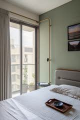 The pipe-integrated bedside table and lamp provide a creative, space-saving lighting solution, reinforcing the room’s modern-rustic charm. The floating side table with a black marble top adds sophistication while maintaining a clutter-free look.