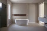 The master bathroom's freestanding tub takes is backdropped by a horizontal bronze accent  that adds depth to the neutral palette.

Natural light filters through the privacy glass window.