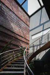 Curved staircase with sleek metal railings and lush indoor greenery, illuminated by natural light from a skylight above.