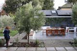 A custom outdoor kitchen with red pizza oven, stainless steel grill, and black soapstone countertops. The dining table and chair are refurbished teak. 