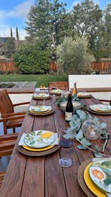 A custom outdoor kitchen with red pizza oven, stainless steel grill, and black soapstone countertops. The dining table and chair are refurbished teak. 