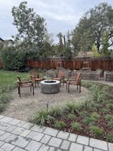 Raised garden beds, surrounding a fire pit, with woven willow siding and a rustic wooden obelisk ,creating a charming and functional vegetable garden design.