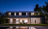A modern house in Israel seamlessly blends minimalist architecture with its natural surroundings, creating a cozy atmosphere through warm lighting, wooden elements, and a smooth transition between indoor and outdoor spaces.