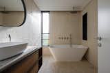 A modern bathroom with natural textures, featuring a freestanding bathtub, a vessel sink, and a large window that allows soft natural light to enter.