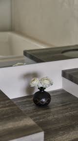 A quiet moment of refinement in the bathroom, where the dark travertine surfaces contrast with a delicate black ceramic vase holding fresh white blooms. The interplay of texture and reflection enhances the sense of depth, embracing wabi-sabi’s appreciation for natural materials and thoughtful simplicity.