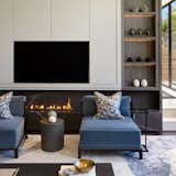 Striking a perfect balance between sleek design and inviting comfort, this modern living area curated by DSI Interiors features a refined palette and strong architectural details. Twin velvet chaises in deep blue anchor the room, paired with geometric accent pillows for a touch of visual interest.

A linear black marble fireplace adds warmth and drama beneath a seamlessly integrated entertainment unit. Built-in shelves with soft backlighting display curated decor elements, lending both character and cohesion to the space. This living room is an effortless blend of form and function—ideal for stylish lounging and elegant entertaining.