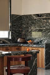Kitchen features bold green-veined marble surfaces, warm wooden cabinetry, and earthy accents, creating a serene yet sophisticated culinary space.








