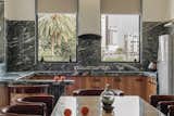Open kitchen and dining space uses striking green marble and warm teak cabinetry to evoke a grounded, sculptural character.