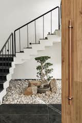 A tranquil entrance court where architecture meets nature—minimalist black madras-and-white stairs float above a Zen-inspired rock garden, anchored by a sculptural bonsai that brings stillness and soul to the heart of the home.