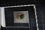 A dramatic top-down view of the staircase block reveals a sculpted choreography of black stone treads spiraling around a central dry court—anchored by a minimalist rock garden that offers a quiet pause within the vertical journey.