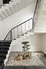 A tranquil entrance court where architecture meets nature—minimalist black madras-and-white stairs float above a Zen-inspired rock garden, anchored by a sculptural bonsai that brings stillness and soul to the heart of the home.