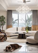 The heart of the home—the living and dining area—has been reimagined to offer both grandeur and intimacy. As one steps inside, banana trees stand as a verdant focal point, forming a striking backdrop that immediately sets a serene tone. A curved feature wall behind the sofa softens the visual experience, reinforcing the flow of the space. The classical ceiling detailing, juxtaposed with sleek, modern furniture, creates a dialogue between tradition and contemporary refinement. 