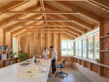 The main workspace is lined with built-in shelving and bathed in natural light. Exposed rafters and studs celebrate standard stick-frame construction, transforming familiar materials into the defining character of the interior.