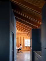 From the kitchenette, a view opens to the main work area where exposed wood framing and daylight define the space. The contrast between deep blue cabinetry and raw wood underscores the studio’s balance of refinement and honesty—while Michael, ever the pensive architect, tries not to giggle as we tell knock knock jokes during the photo shoot.