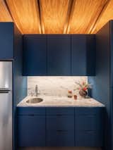 The compact kitchenette combines deep blue cabinetry and quartz counters, echoing the project’s balance of raw and refined materials. Wood framing remains visible above, reinforcing the studio’s honest construction approach.