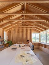 Large windows bring daylight deep into the workroom, while exposed wood structure offers both visual warmth and a constant reminder of the building’s construction logic. The long table supports collaborative design work in a compact footprint.