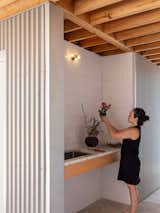 An outdoor sink tucked beneath the porch roof serves both practical and informal uses, from gardening to cleanup. White tile, exposed wood, and corrugated siding continue the project’s material palette of straightforward, durable finishes.