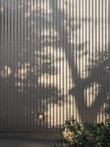 Early morning light casts tree shadows across the Galvalume siding, emphasizing its subtle texture and connection to the site. The exterior cladding’s durability and reflectivity make it both practical for Texas heat and evocative of rural vernacular buildings.