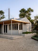 The porch canopy is framed with exposed wood and supported by galvanized fence posts sourced from a local feed store—an economical, readily available material choice. Together with the corrugated siding, concrete steps, and low planter, these elements form a welcoming and straightforward entry sequence.