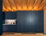 The kitchenette pairs deep blue cabinetry with a quartz backsplash, introducing a refined counterpoint to the otherwise raw wood interior. Tall storage integrates an all-in-one washer/dryer and maximizes the compact footprint’s utility.