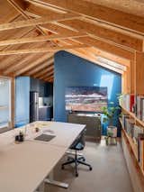 The work table anchors the open workroom, with built-in shelving on one side and a deep blue feature wall on the other. This color, repeated in the kitchenette cabinetry, adds contrast and focus within the otherwise raw wood interior.