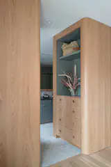 A soft transition from the primary bedroom to the ensuite is framed by curved corners in the white oak built-in, creating a sense of flow and calm. Custom-milled pulls are seamlessly integrated into the cabinetry, adding a tactile, tailored finish to the warm woodwork.