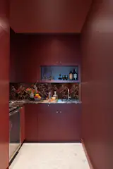 A moody, jewel-toned retreat: the wine room is fully saturated in a custom maroon-berry hue, wrapping walls, trim, and ceiling in a single, immersive tone. A striking rosso Italian marble countertop and backsplash add depth and drama, while the integrated wet bar offers both function and flair.