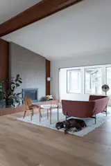 The original mahogany wall, trim, and vaulted ceiling beam were preserved to honour the home's mid-century soul. The existing brick fireplace, which once stopped at the mantle, was replaced with a floor-to-ceiling tile surround and a sleek gas insert. A new full-length hearth anchors the room, drawing the eye across the space and tying the expansive layout back to the warmth of the original mahogany.