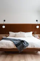 In the primary bedroom, a custom upholstered headboard in rusty berry velvet adds depth and warmth, setting a soft, grounded tone for the space. The bay window overlooks a private, tree-filled yard—so lush and secluded that no blinds are needed, just the natural privacy of the surrounding woods.