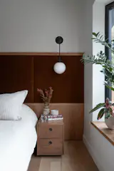 In the primary bedroom, a custom upholstered headboard in rusty berry velvet adds depth and warmth, setting a soft, grounded tone for the space. The bay window overlooks a private, tree-filled yard—so lush and secluded that no blinds are needed, just the natural privacy of the surrounding woods.