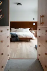 A soft transition from the primary bedroom to the ensuite is framed by curved corners in the white oak built-in, creating a sense of flow and calm. Custom-milled pulls are seamlessly integrated into the cabinetry, adding a tactile, tailored finish to the warm woodwork.