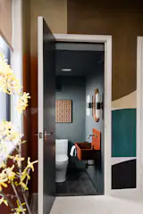 A view from the mural-wrapped home office reveals a jewel-box powder room layered in texture. The space features a custom terracotta concrete sink, brass fixtures, and textured wallpaper that adds warmth and depth.